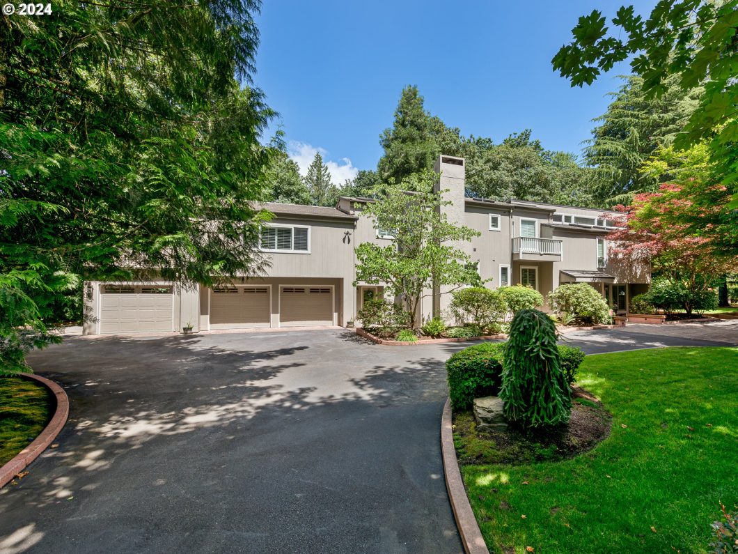 A large contemporary house with a three-car garage, surrounded by lush greenery.