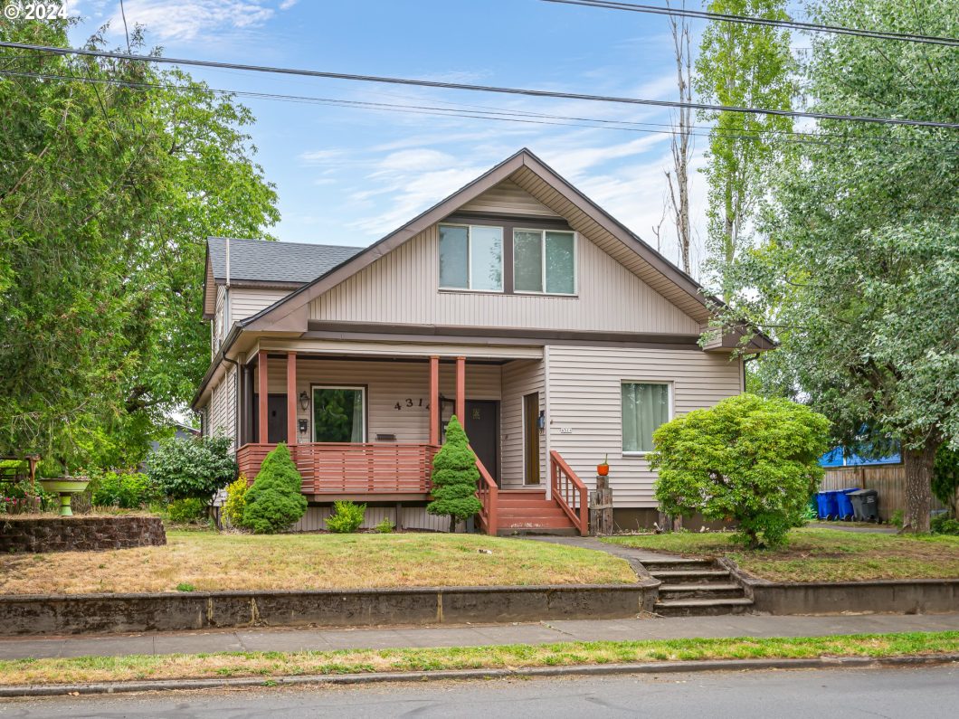 A classic two-story house with a covered front porch and neatly trimmed bushes in the front yard.