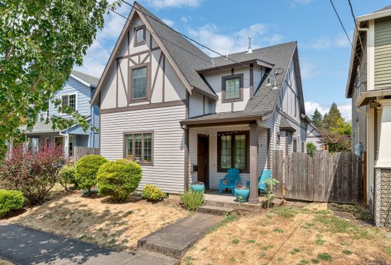 Modern gray house with a sloped roof, three-car garage, and large front yard on a sunny day.