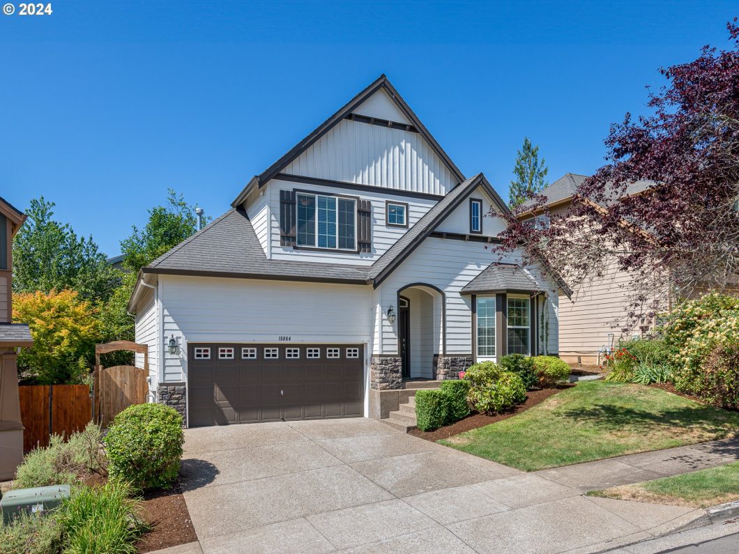 A two-story house with a white and gray exterior, a steep roof, and well-maintained front yard.